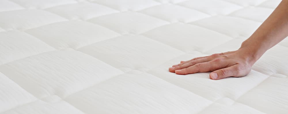Close-up of a hand checking the firmness of a mattress, used to represent signs you need a new mattress for better comfort and sleep health.